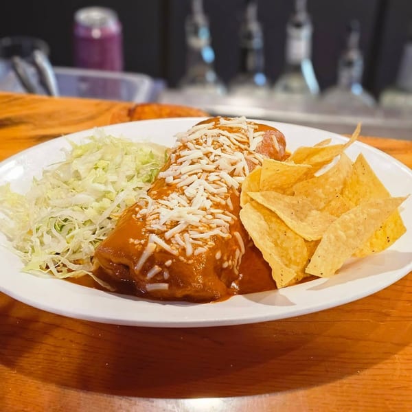 A Nuestro Sabor burrito covered in red sauce and cheese, with shredded lettuce and tortilla chips.
