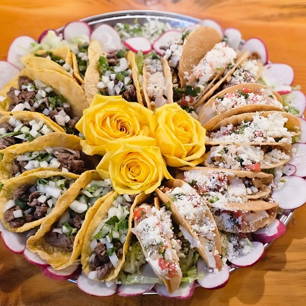 A platter of Nuestro Sabor tacos, some with meat and onions, others with cheese and pico de gallo.