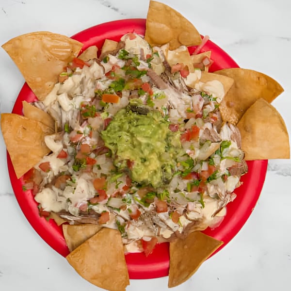 Nachos with meat, white sauce, pico de gallo, and guacamole on a red plate.