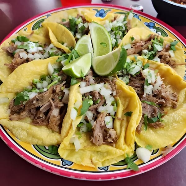 A colorful plate of Nuestro Sabor's Mexican tacos, topped with shredded meat, onions, cilantro, and lime wedges.