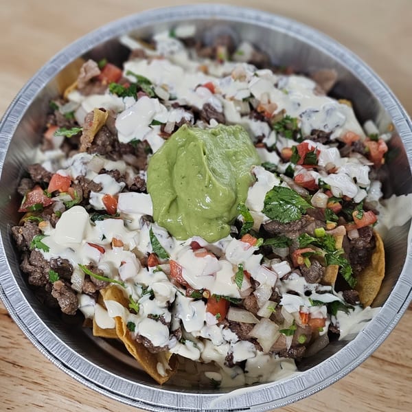 Mexican nachos with steak, pico de gallo, sour cream, and guacamole in a foil container.