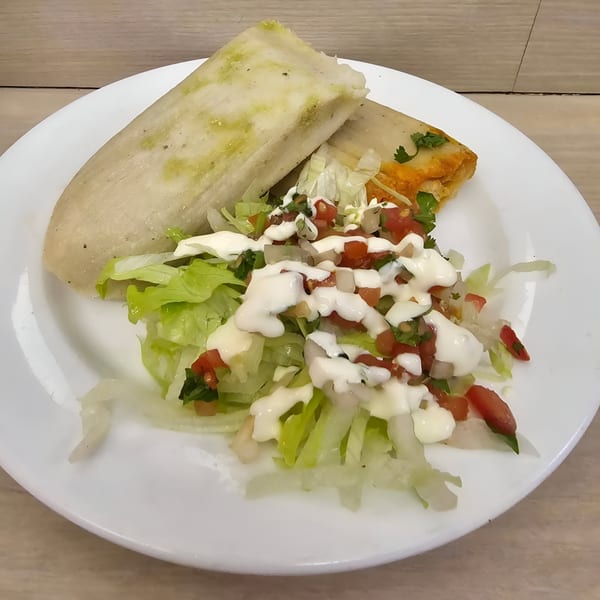 Two Nuestro Sabor tamales, one green and one orange, served with a side salad topped with dressing.