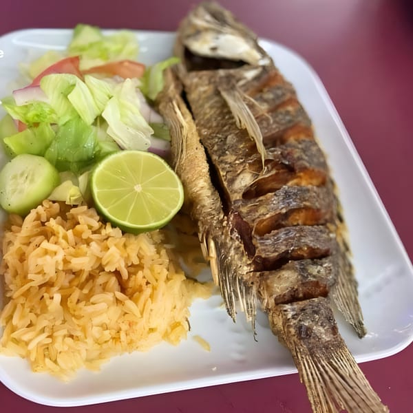 Whole fried fish with rice, salad, and a lime wedge on a white plate at Nuestro Sabor.